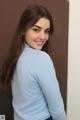 A woman in a blue shirt leaning against a wall.