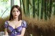 A woman in a purple dress sitting in front of a bamboo tree.