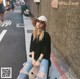 A woman sitting on a suitcase on the side of a street.
