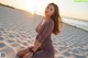 A woman sitting on a sandy beach at sunset.