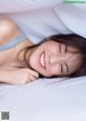 A woman laying in bed with her eyes closed and smiling.