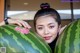 A woman holding two large watermelons in front of her face.