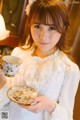 A woman in a white dress holding a cup and saucer.